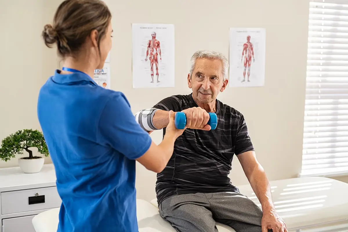 Physiotherapeutin übt mit einem älteren Patienten mit Hanteln